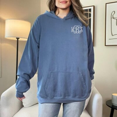 A woman standing in a room, wearing a blue hoodie with a monogram design.