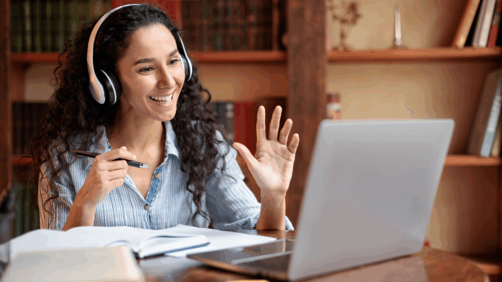 A woman in headphones sitting in front of a laptop and teaching online.