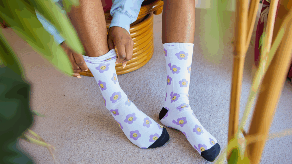 A woman displays her socks featuring a cheerful flower pattern, adding a playful touch to her outfit.