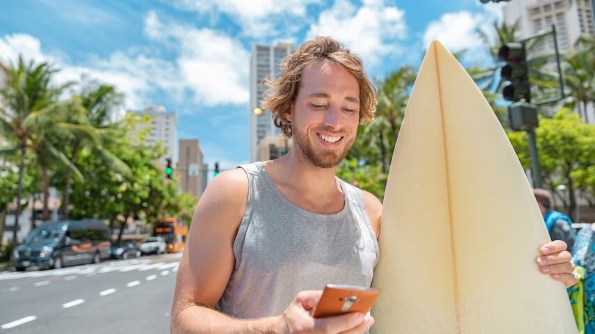 Australian man looking at his phone while holding a surfboard.