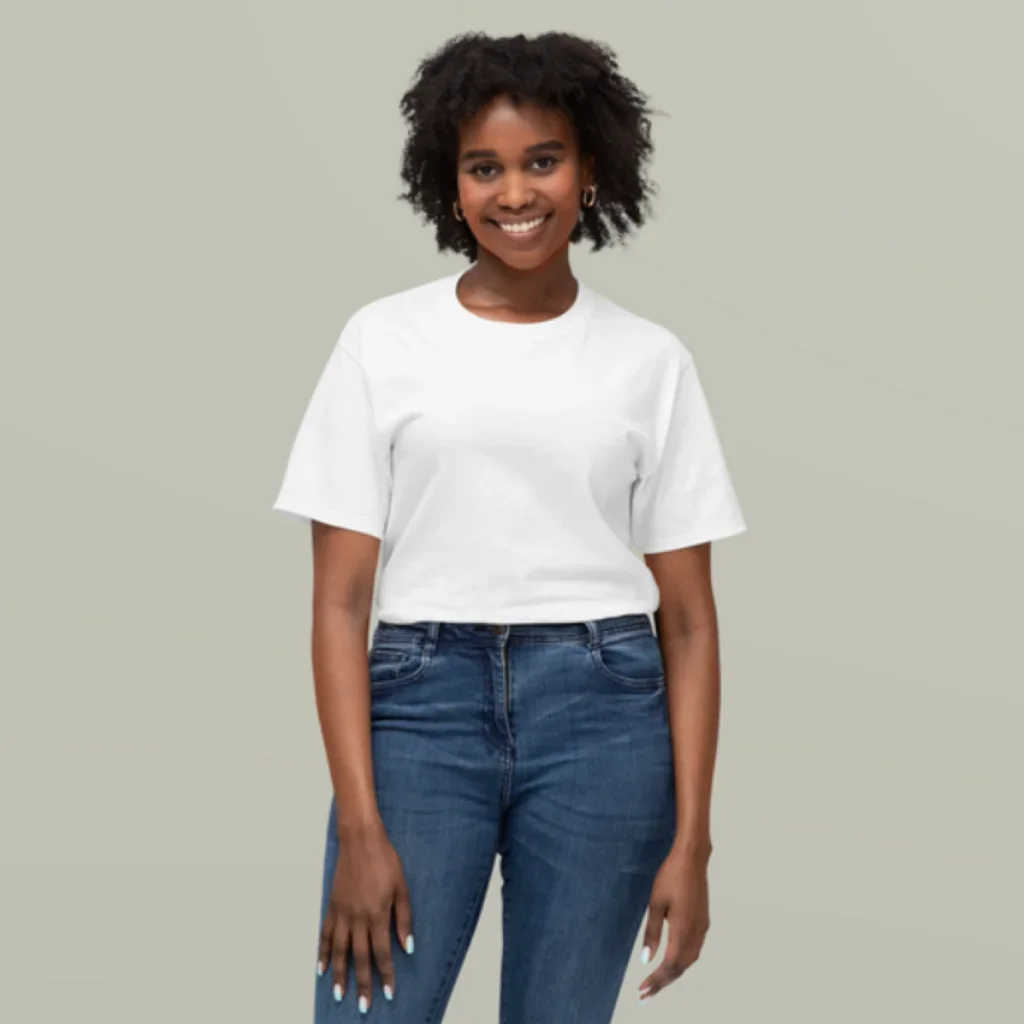 Smiling person with curly hair wearing a white T-shirt and blue jeans, standing against a plain gray background, exuding confidence and warmth.