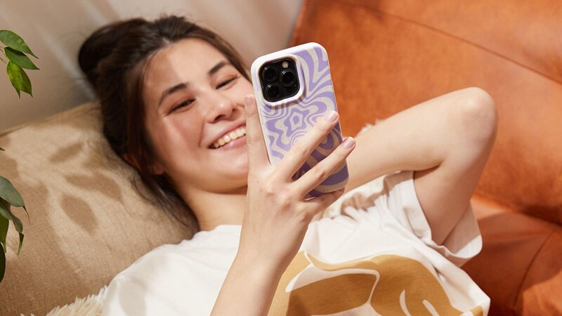 A young woman lying on a couch and smiling while looking at her phone, reading a comparison article: TikTok Shop vs Etsy.