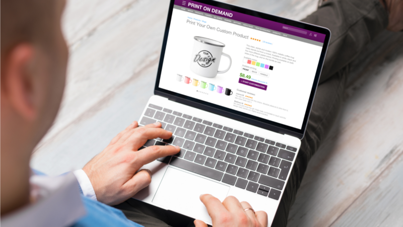 A person is using a laptop featuring a "Print on Demand" website.