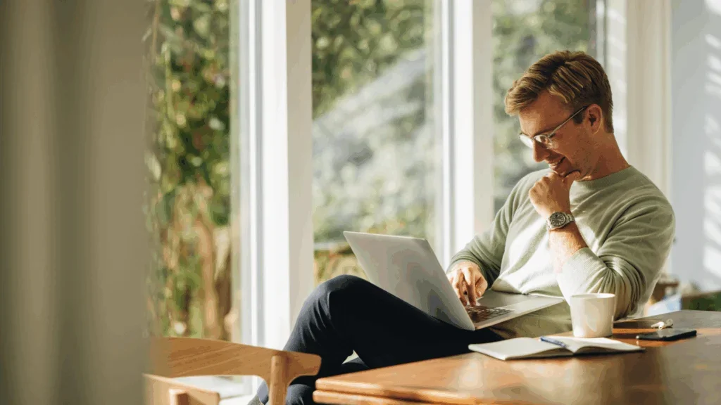 A man seated at a table, focused on his laptop.