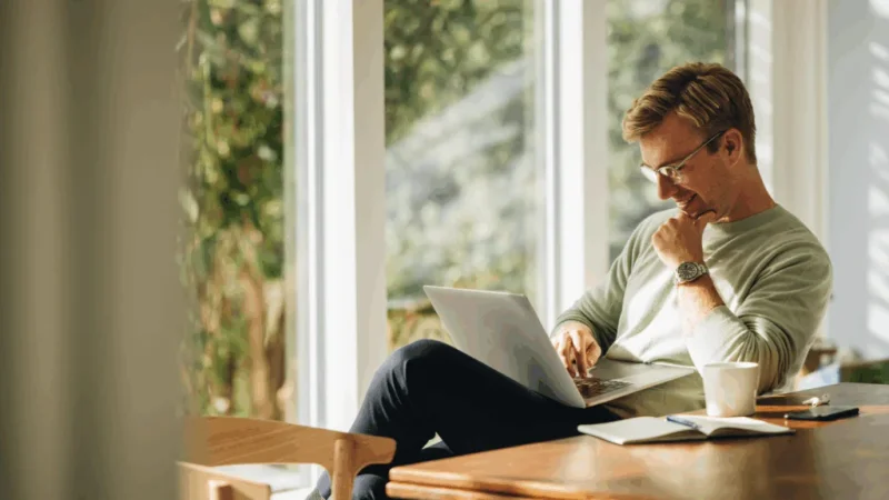 A man seated at a table, focused on his laptop.