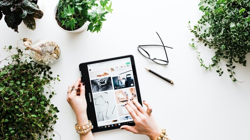 A tablet on the table with hands around it, flowers on the table.