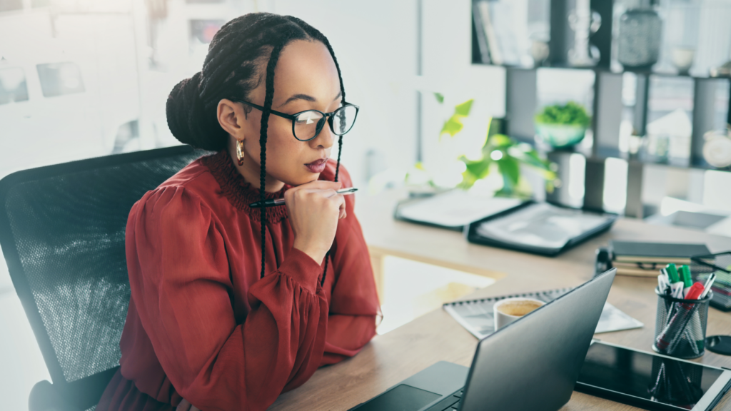 A woman sitting in an office environment and reading from a laptop the latest on tariffs.