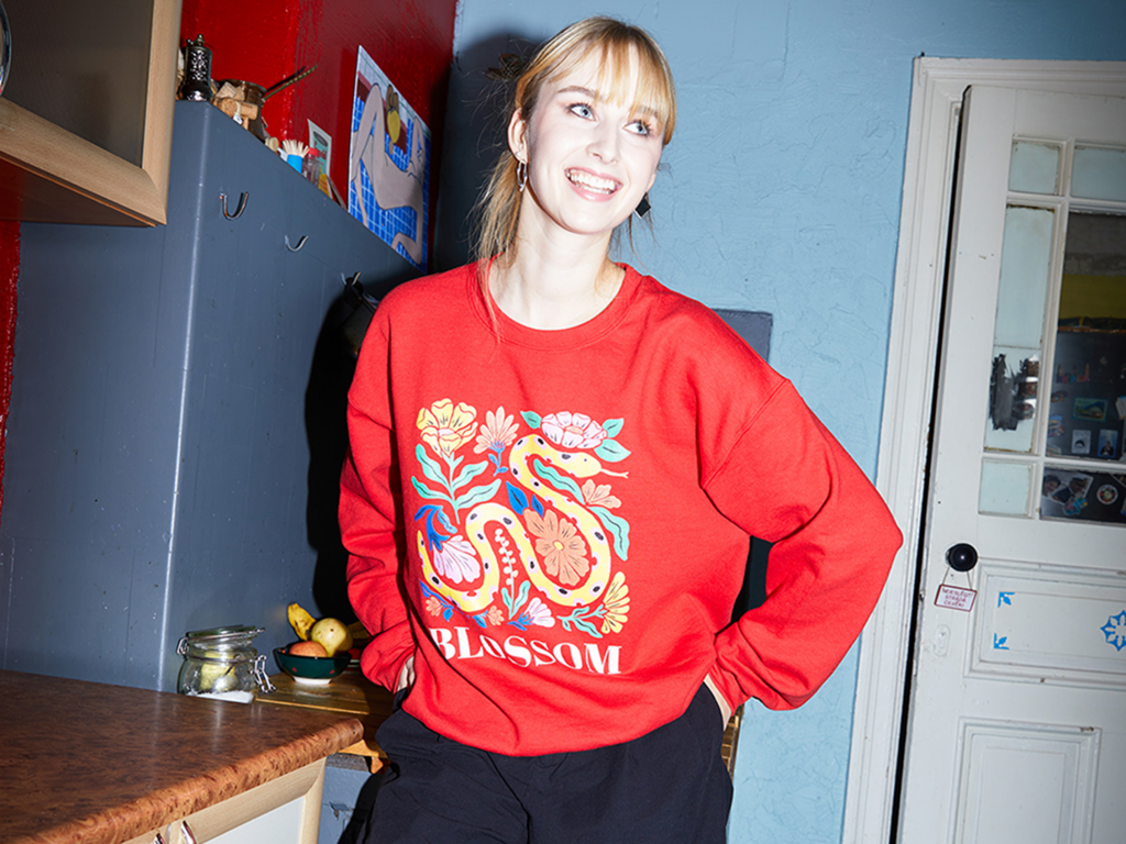 A woman in a custom-printed sweatshirt stands in a modern kitchen, surrounded by appliances and natural light.