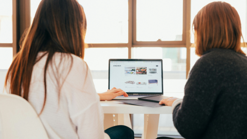 Two women sitting in front of a laptop and adjusting a website.