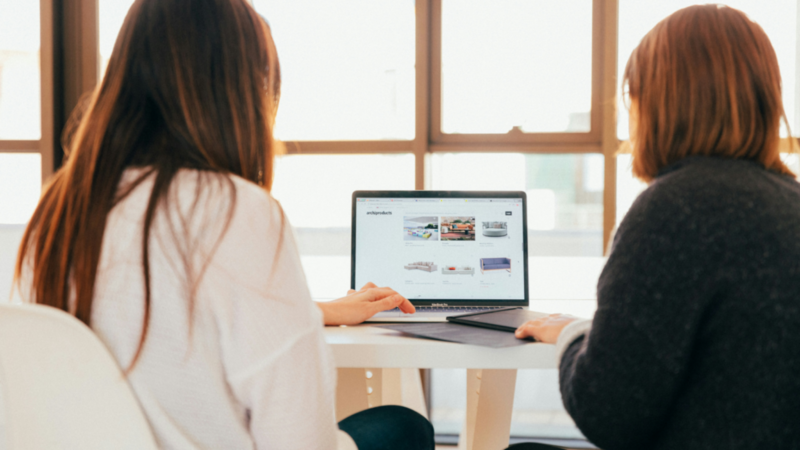 Two women sitting in front of a laptop and adjusting a website.
