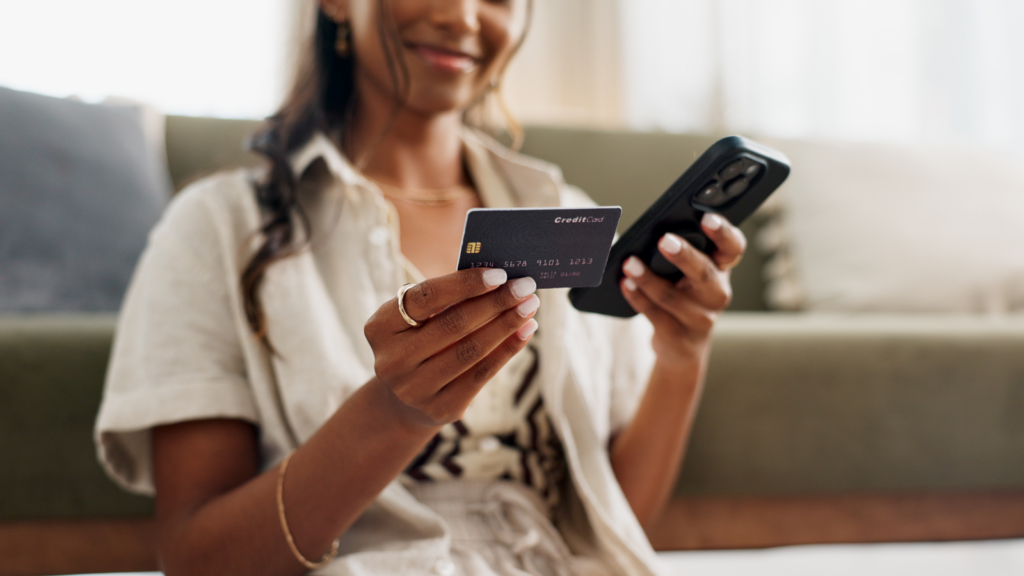A woman holding a phone in one hand and a credit card in the other.