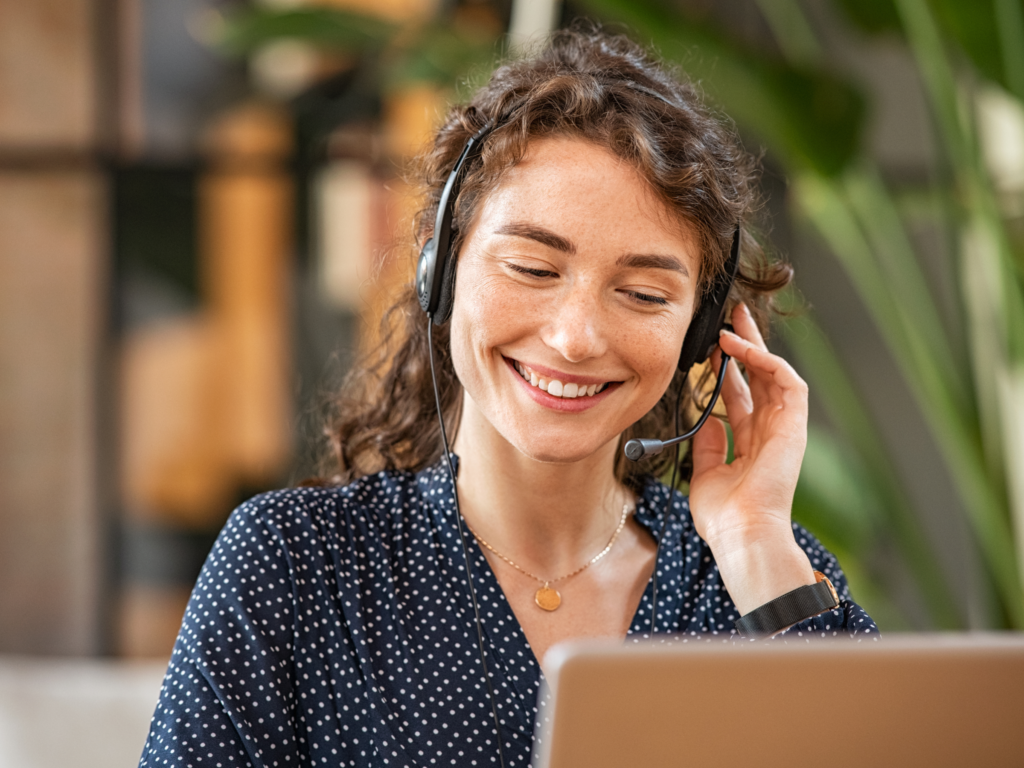A woman smiling and speaking on the phone as a customer support agent.