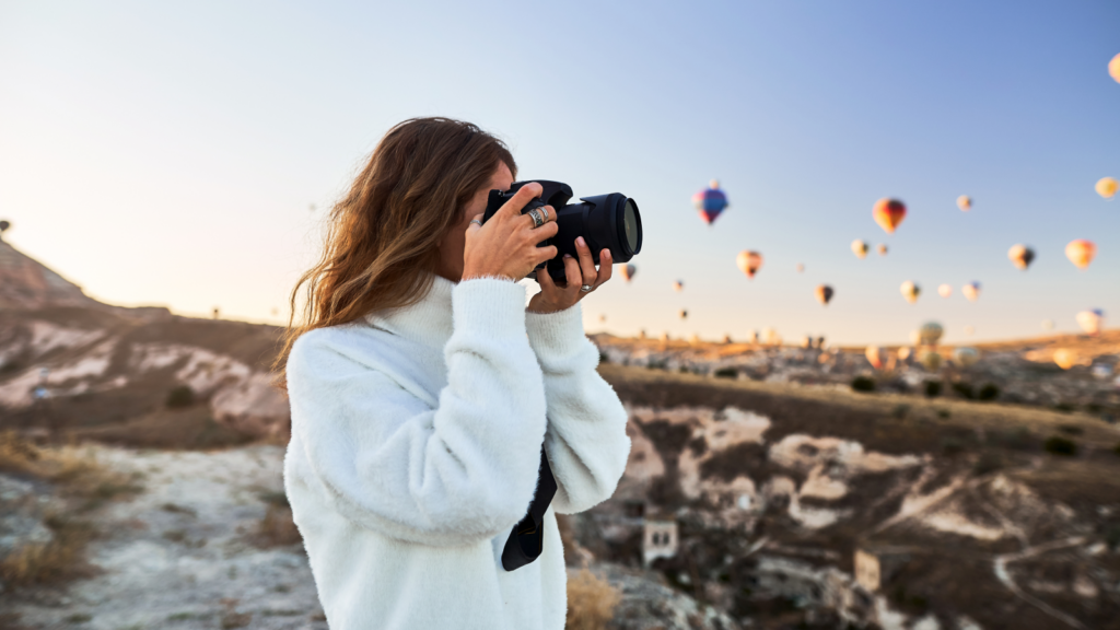 A woman photographs vibrant hot air balloons floating gracefully above the unique terrain of Cappadocia.