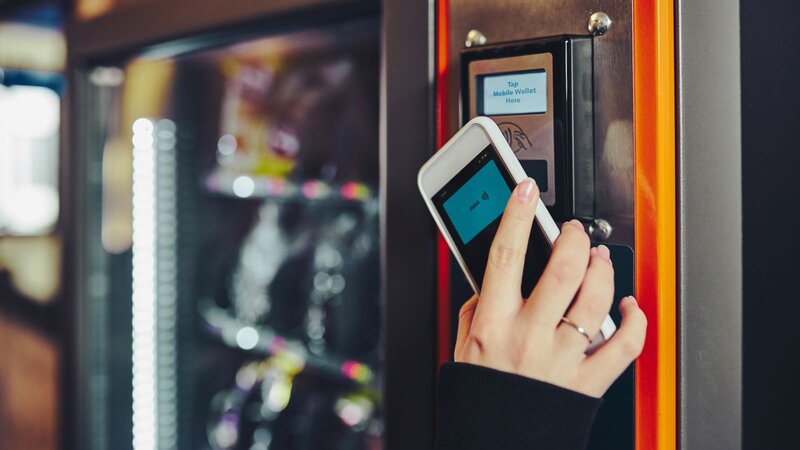 A person using a mobile device to pay for something at a vending machine.