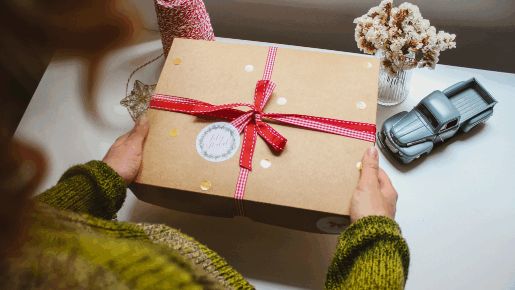 A woman holding a wrapped gift box, smiling, with a table in the background.