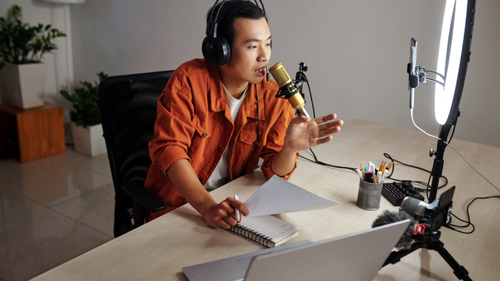 A man wearing headphones sits at a desk, focused on his laptop and microphone, ready for a recording session.