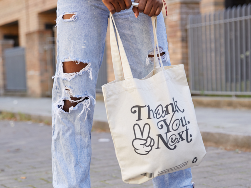 A woman in ripped jeans carries a tote bag that reads "Thank you next".