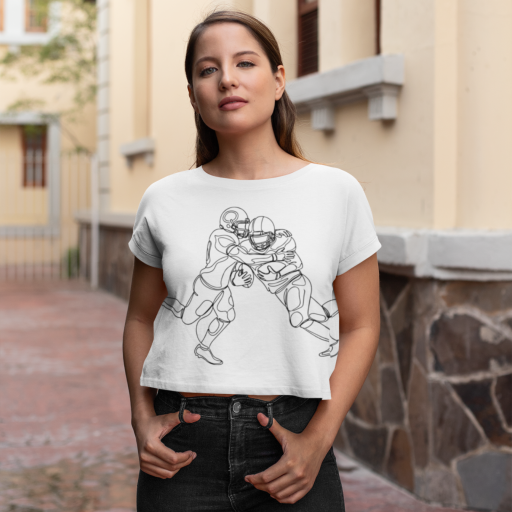 A woman wearing a white crop top with a sketch design of two American football players. She stands confidently in an urban setting.
