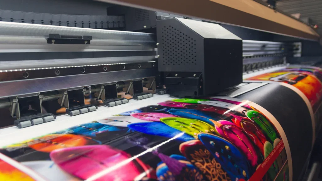 A large print machine actively printing a large sheet of paper with text and images.