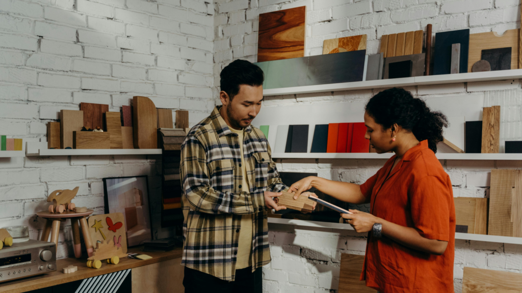 A man and a woman passing a handmade product from wood.