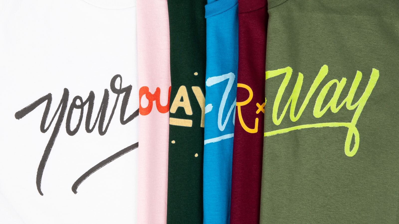 A stack of different t-shirts, put together, with the text “Your way” in different colors and fonts.
