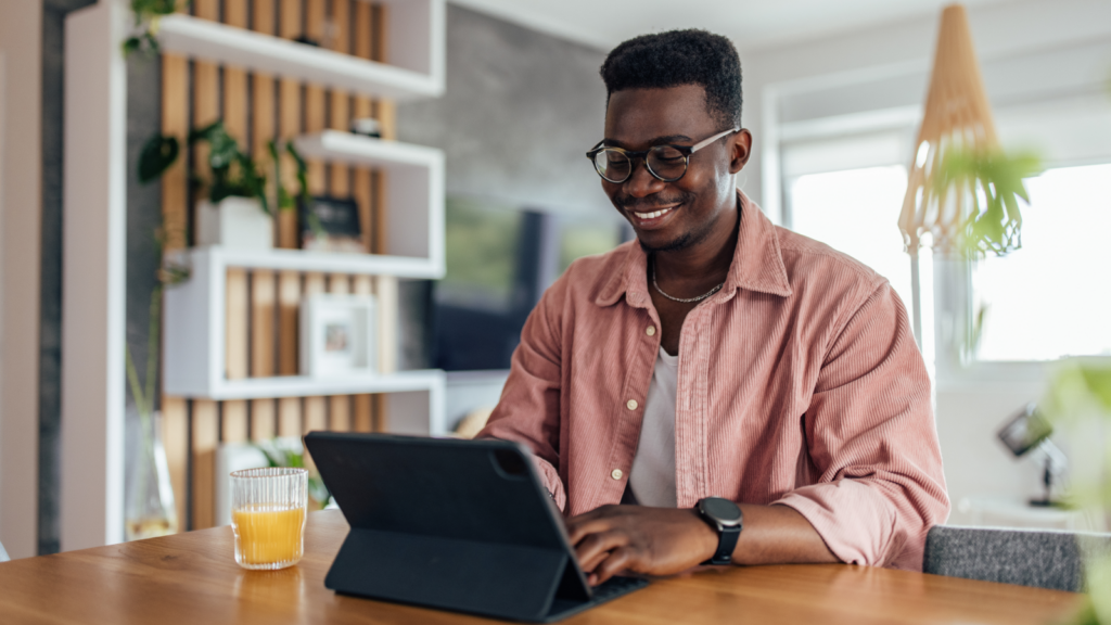 A man sitting at a table, working on a tablet, and drinking orange juice.