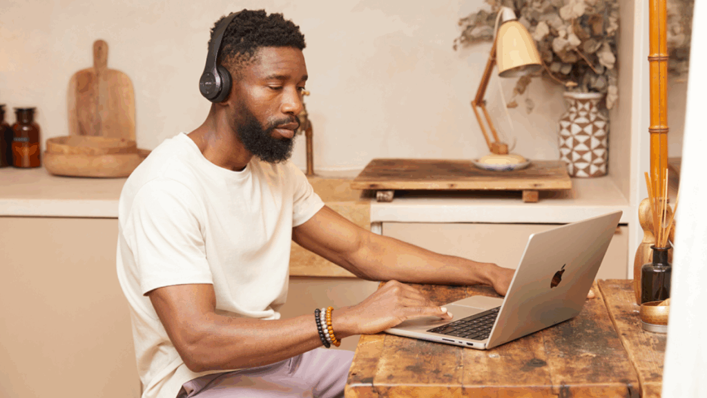 A man is sitting at a kitchen table and using a laptop.
