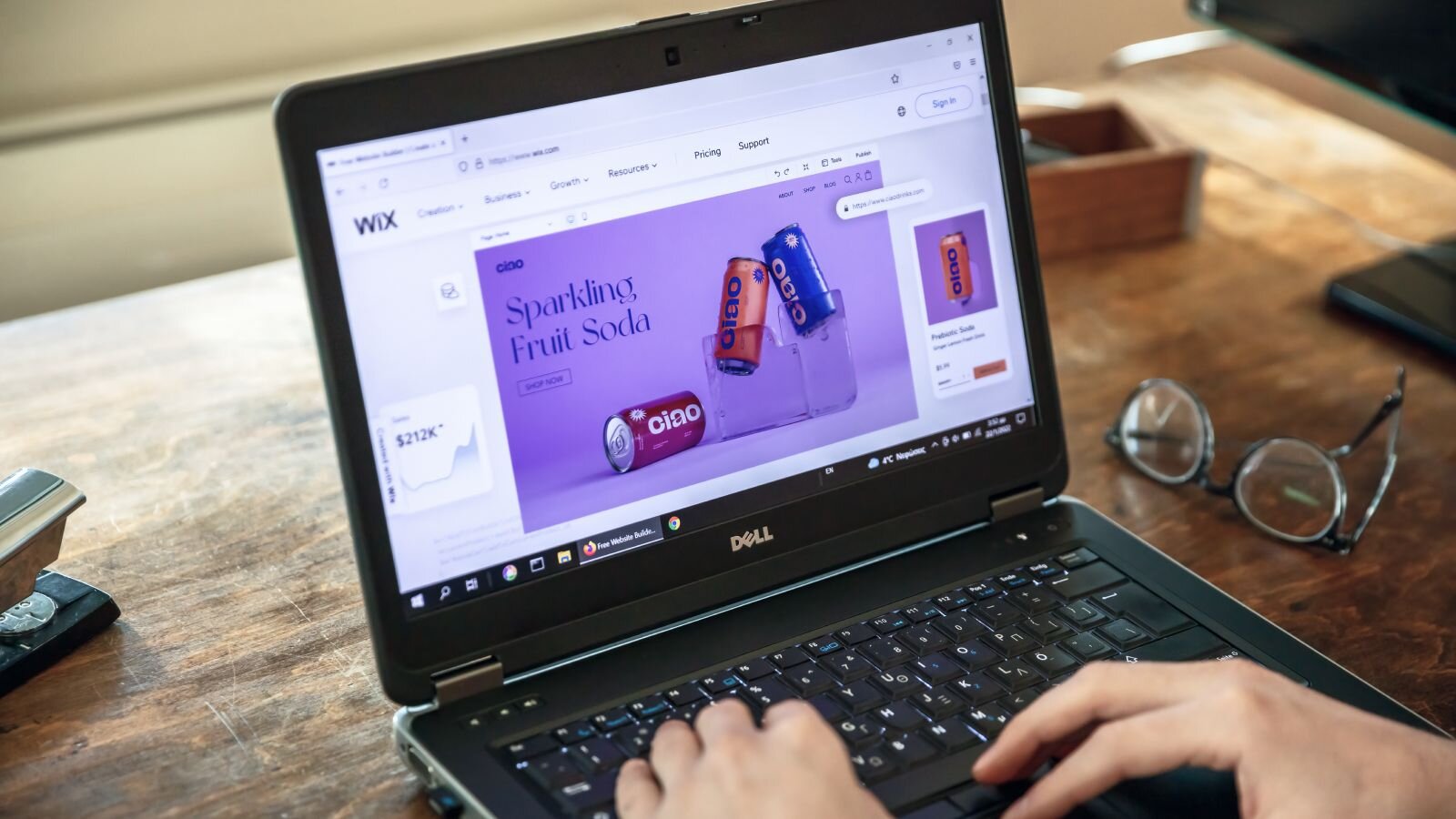 A person working on a laptop displaying a Wix webpage featuring sparkling fruit soda cans on a purple background.