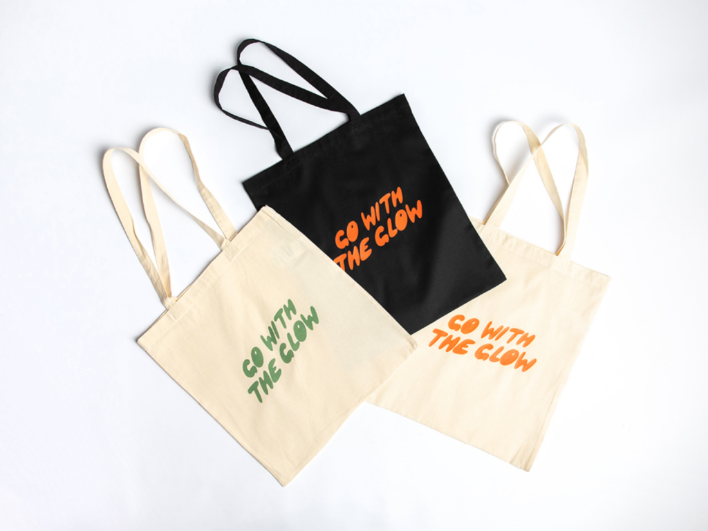 Three custom “Go with the Glow” tote bags in multiple colors on a white background.