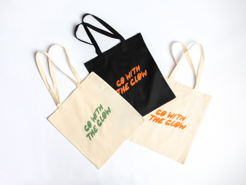 Three custom “Go with the Glow” tote bags in multiple colors on a white background.
