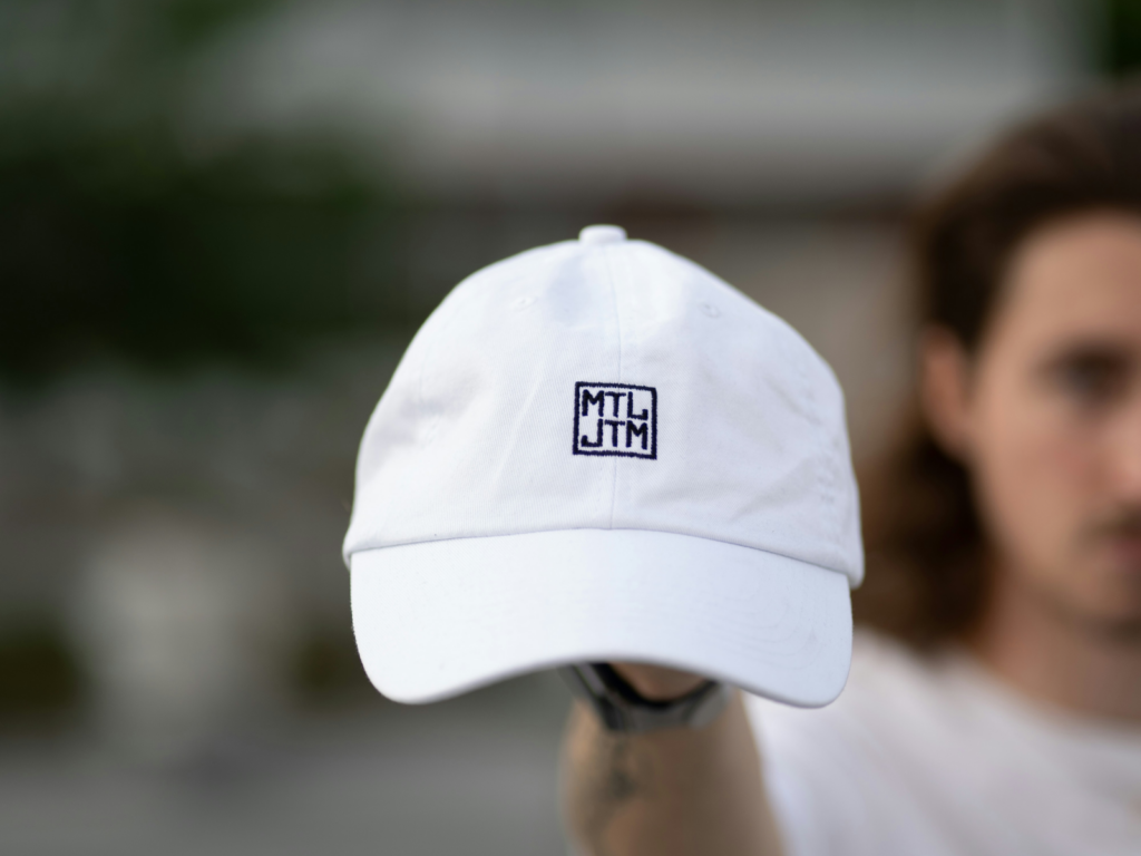 A man holding a white cap with a black “MTLJTM” logo.