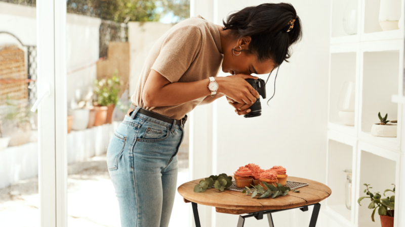 A woman photographing a cupcake on a table, capturing the dessert's details with her camera.