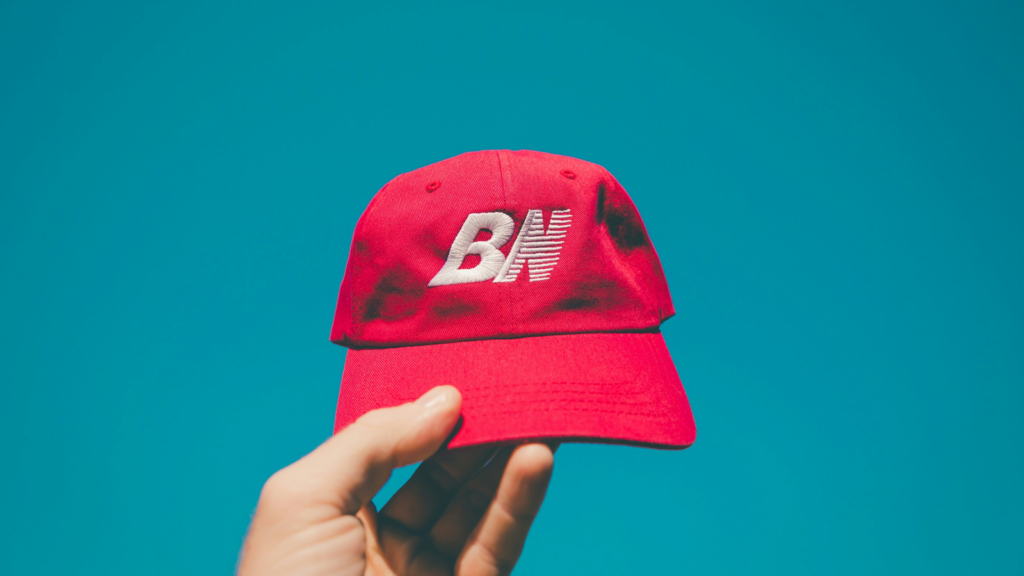 A person holding a red hat with a white logo on a blue background.