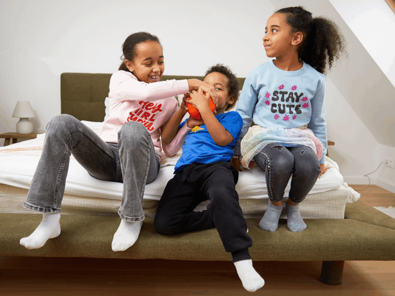 A group of kids (2 girls, 1 boy) playing on a bed.