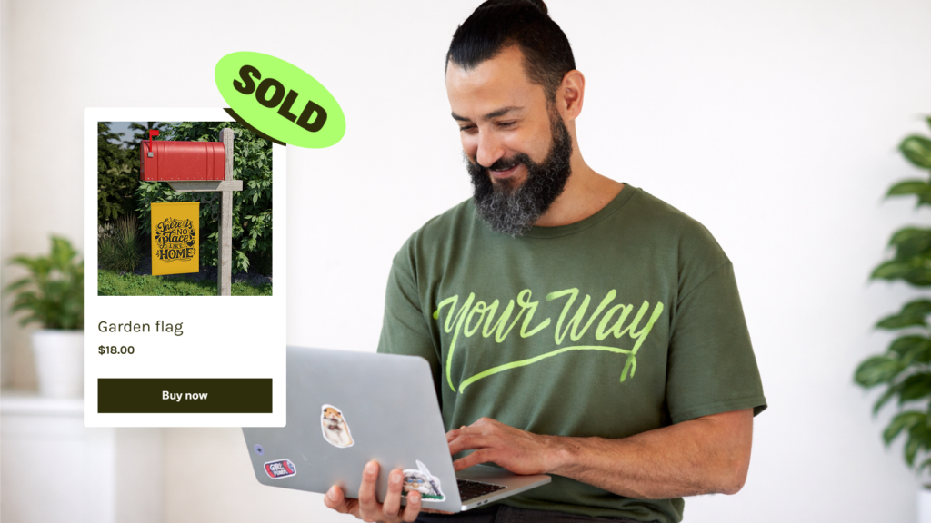 A man with a beard smiles while using a laptop. An image of a garden flag with a "SOLD" tag is shown.