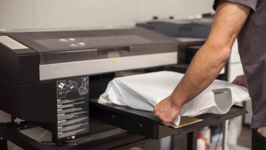 A man using a direct-to-garment printing machine on a white shirt.
