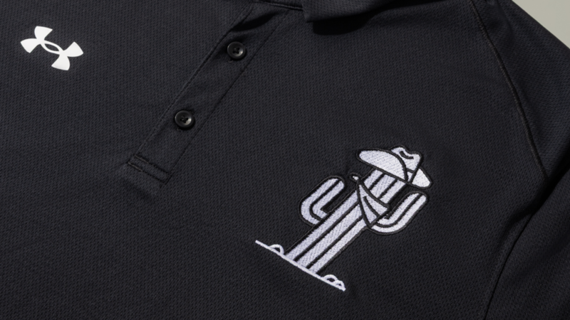 A close-up of a black polo shirt featuring a cactus logo and an Under Armour logo on the left chest area.