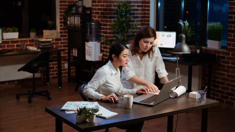 Two women looking at a laptop screen in an office environment.
