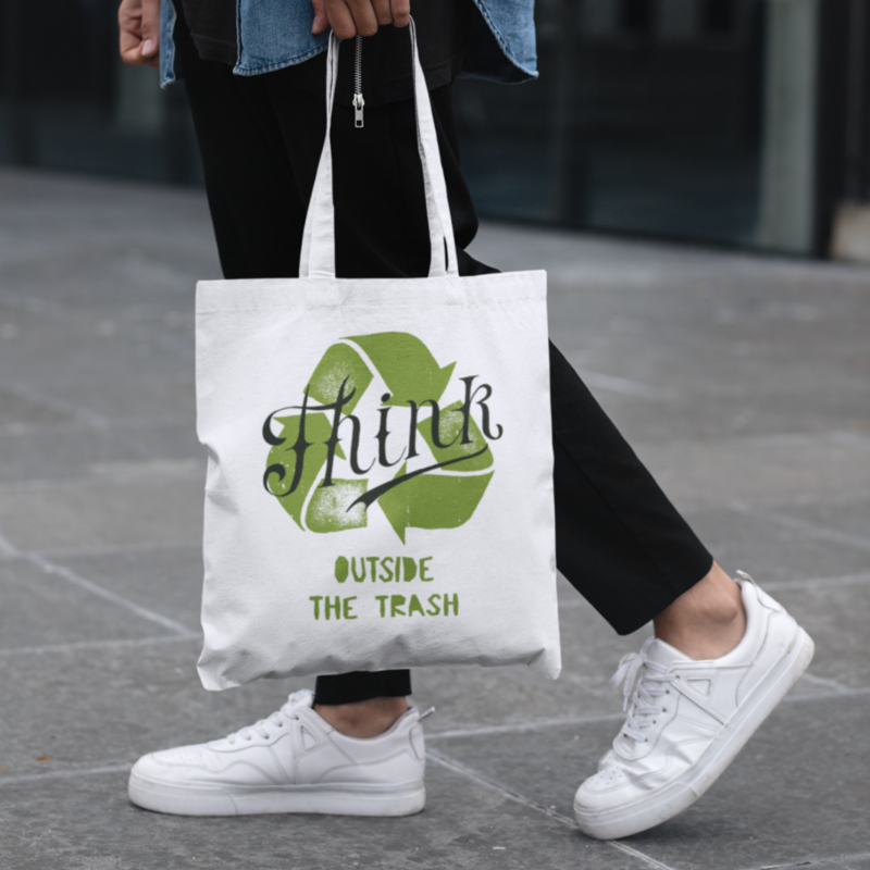 A person walking in the streets, wearing a custom “Think outside the trash” tote bag.