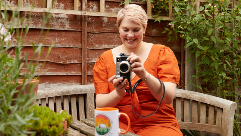 A young woman in an orange dress is taking a picture of a custom mug.