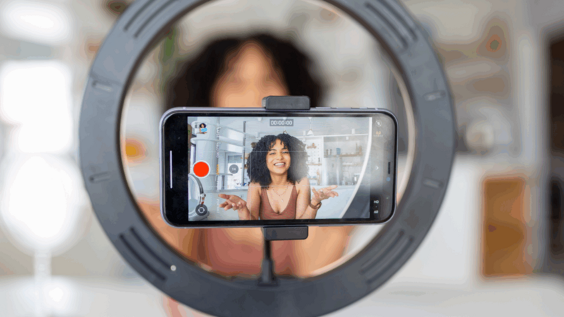A young woman recording herself using a mobile phone on a tripod.