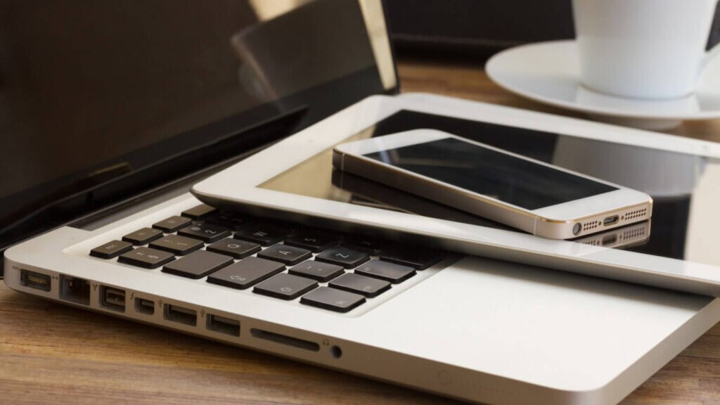 A laptop, tablet, and cell phone stacked on top of each other.