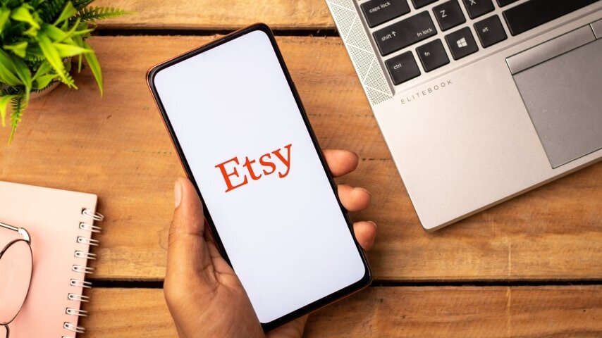 A person holding a phone with the Etsy logo displayed on the screen.