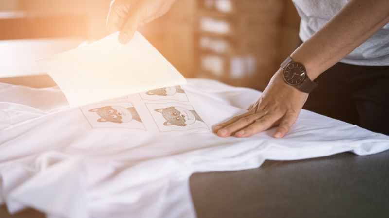 Hands peel transfer paper off a printed white T-shirt.