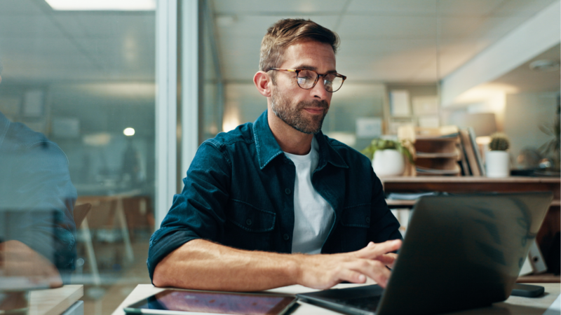 A man working on a laptop at a desk, learning how to sell digital planners on Etsy.