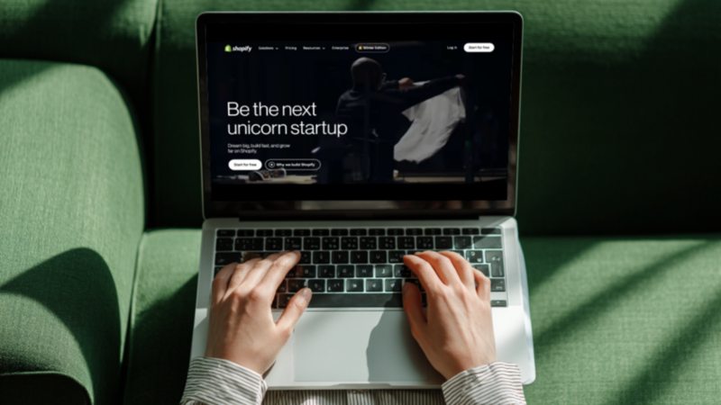 A person is using a laptop with Shopify’s homepage on the screen.