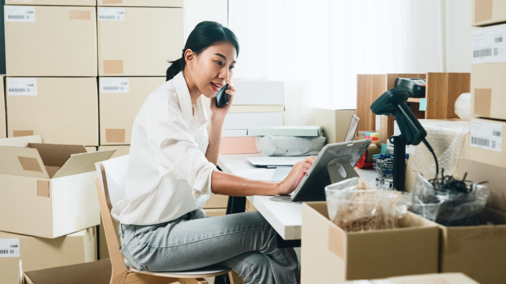 A woman is talking on the phone and working on a laptop.