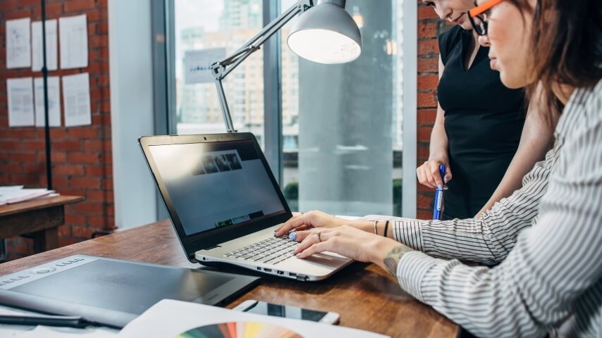 Two women designing an image on a laptop.