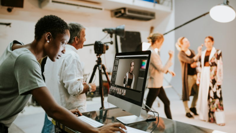 A photographer edits a portrait on a computer in a bustling studio.