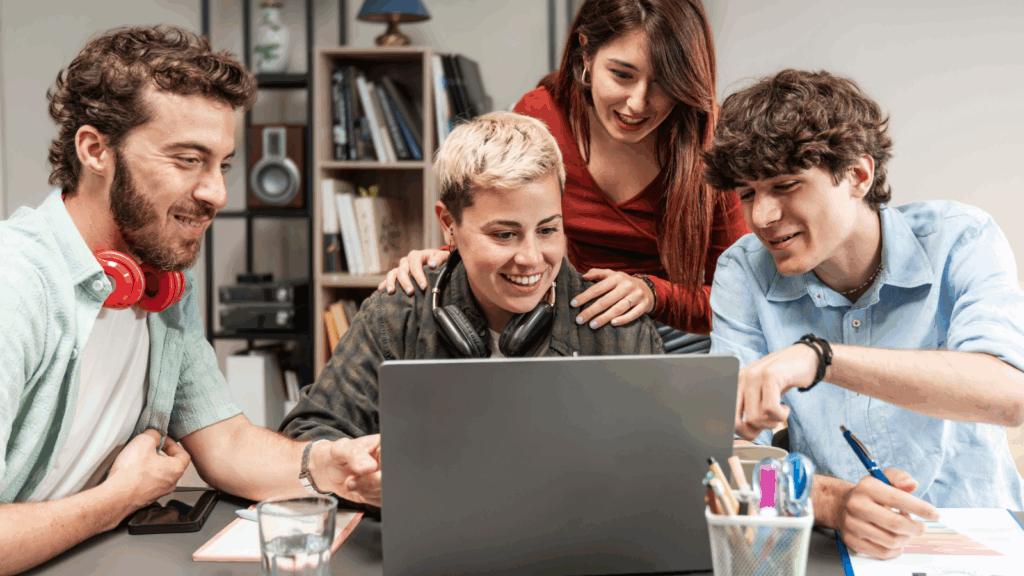 Four young people gather around a laptop, intently focused on the screen as they discuss its content.